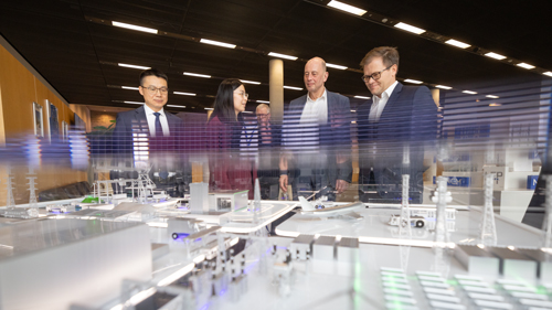 Gruppe von Personen, darunter ein Politiker und Geschäftsleute, betrachten interaktiv ein detailliertes Architekturmodell eines Industriekomplexes in einem gut beleuchteten Ausstellungsraum.