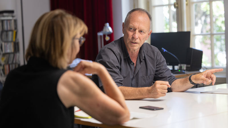 Hasko Weber sitzt an einem Tisch in seinem Büro und führt ein intensives Gespräch mit Susanne Stiefel. Er gestikuliert mit einer Hand, während er spricht.