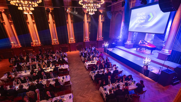 Festlich gedeckter Saal mit Teilnehmenden des Europäischen Commercial Summit, Bühne mit „Ready, Steady, Grow!“-Leinwand im Hintergrund.