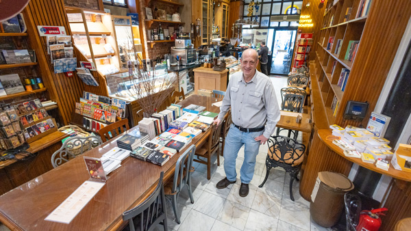 in Buchhändler steht in einem gemütlichen Laden in Istanbul, umgeben von Büchern und Tischen. Die Atmosphäre ist einladend, mit warmem Licht und einem Hauch von Tradition.