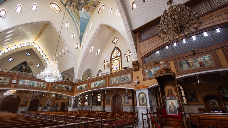 Prächtig verzierter Innenraum einer Kirche mit Kronleuchtern, Wandgemälden und Holzbänken unter einem gewölbten Deckenfresko.