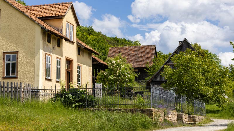 Historisches Bauernhaus mit Fachwerk und Garten vor blauem Himmel in ländlicher Umgebung.