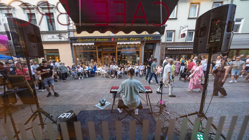 Straßenmusiker spielt Keyboard vor einem Café, viele Zuschauer auf der Fußgängerzone.