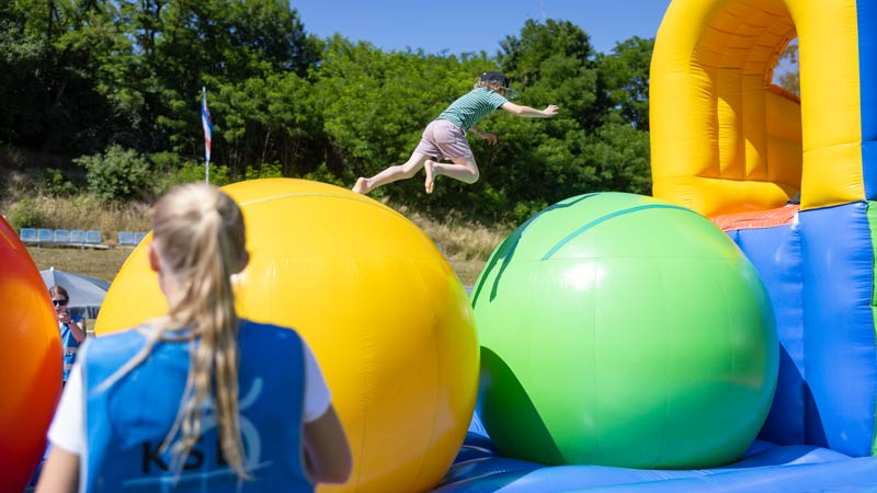 Kind springt auf einem Hüpfparcours mit großen bunten Bällen im Freien.