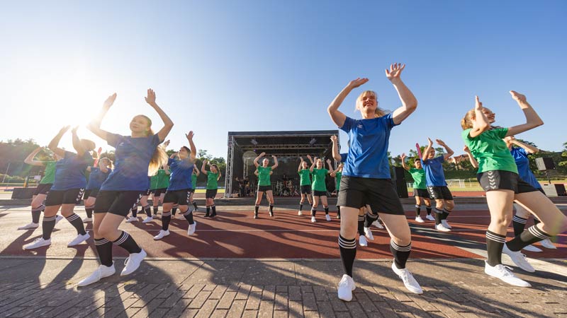 Tanzgruppe in Sportkleidung führt Choreografie vor Bühne im Freien auf.