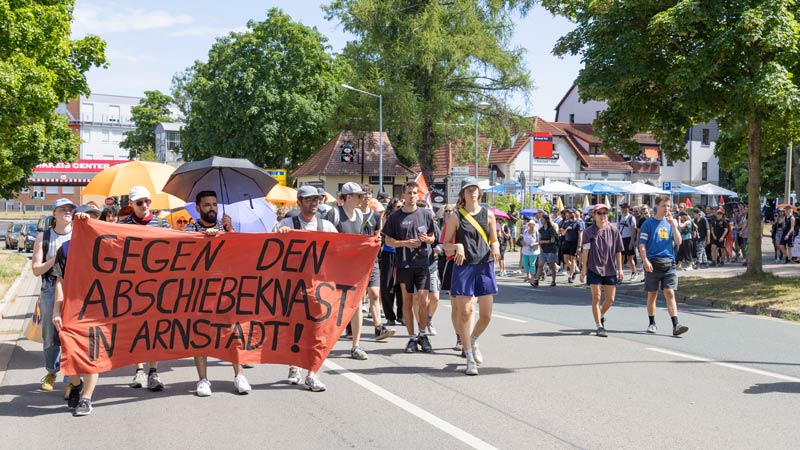 Demonstrierende laufen mit rotem Banner „Gegen den Abschiebeknast in Arnstadt!“ über eine Straße.