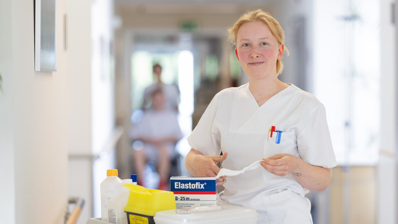 Krankenschwester mit Verbandmaterial an einem Versorgungswagen im Krankenhausflur.