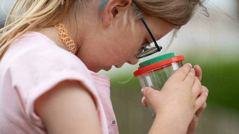 Mädchen mit Brille schaut konzentriert in einen transparenten Becher mit rotem Deckel.