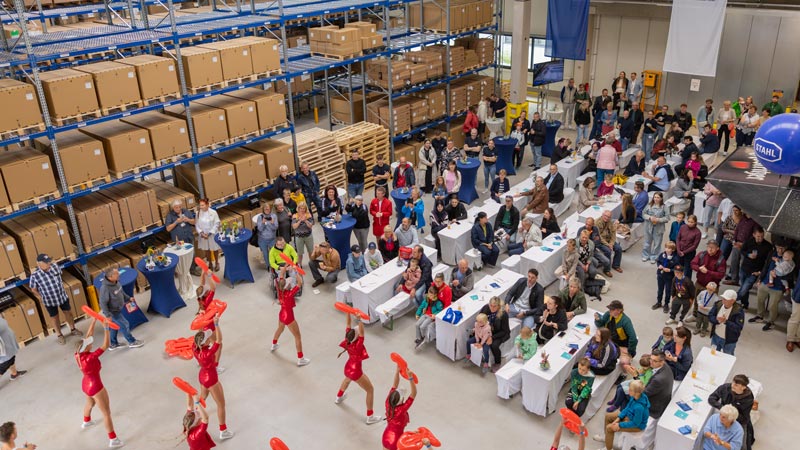 Innenaufnahme einer Lagerhalle mit Publikum und Cheerleaderinnen bei Firmenveranstaltung.