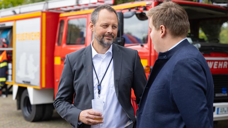 Zwei Männer im Gespräch vor einem roten Feuerwehrfahrzeug