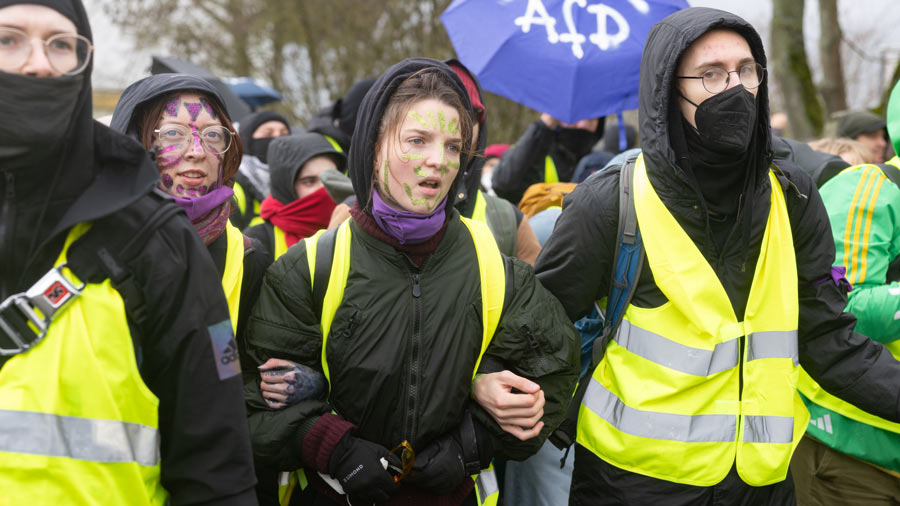 Junge Demonstrierende mit gelben Westen und bemalten Gesichtern laufen Arm in Arm bei einem Protest