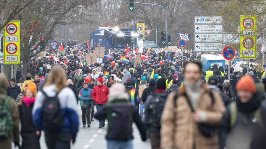 Dichter Demonstrationszug mit Bannern, Schildern und Polizeifahrzeugen im Hintergrund