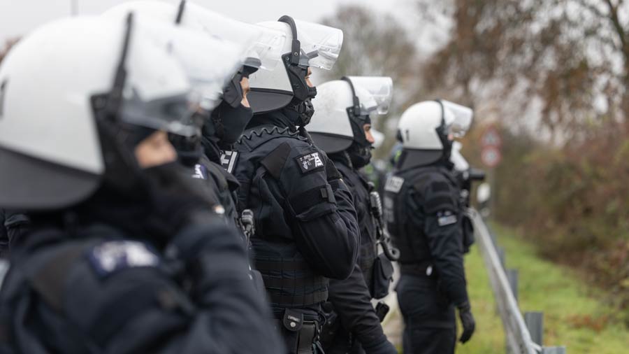 Polizist*innen in schwerer Schutzmontur stehen in Reihe während eines Protests