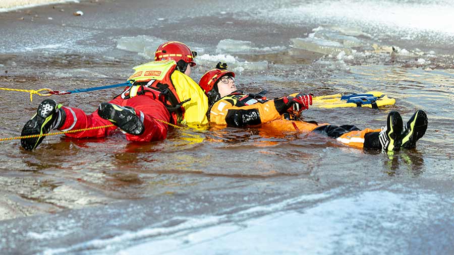 Retter zieht verletzte Person in Überlebensanzug aus einem Eisloch zur Sicherheit.