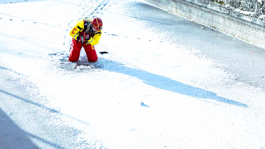 Eine Rettungskraft kniet auf einer gefrorenen Fläche und hält ein Sicherungsseil.