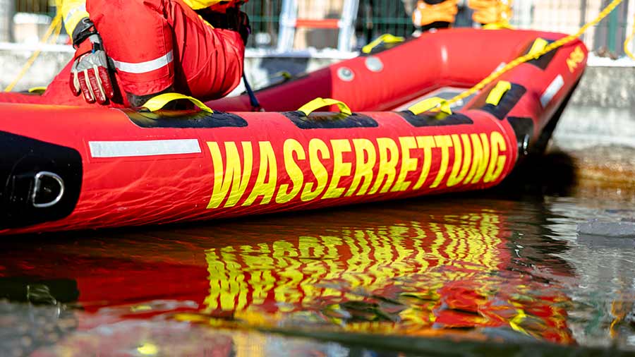 Aufschrift „WASSERRETTUNG“ auf einem roten Schlauchboot der DLRG spiegelt sich im Wasser.