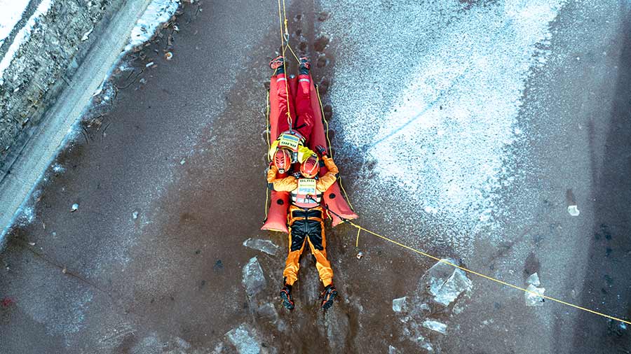 Zwei Rettungskräfte seilen sich mit einer Trage über eine vereiste Wasserfläche ab.