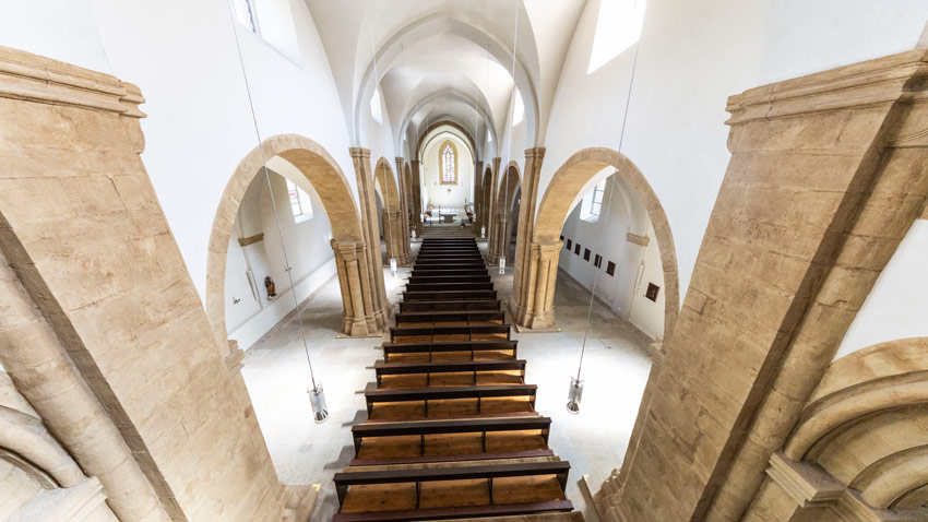 Blick von oben in das Kirchenschiff einer gotischen Kirche in Erfurt, hölzerne Kirchenbänke und helle Spitzbogen-Architektur.