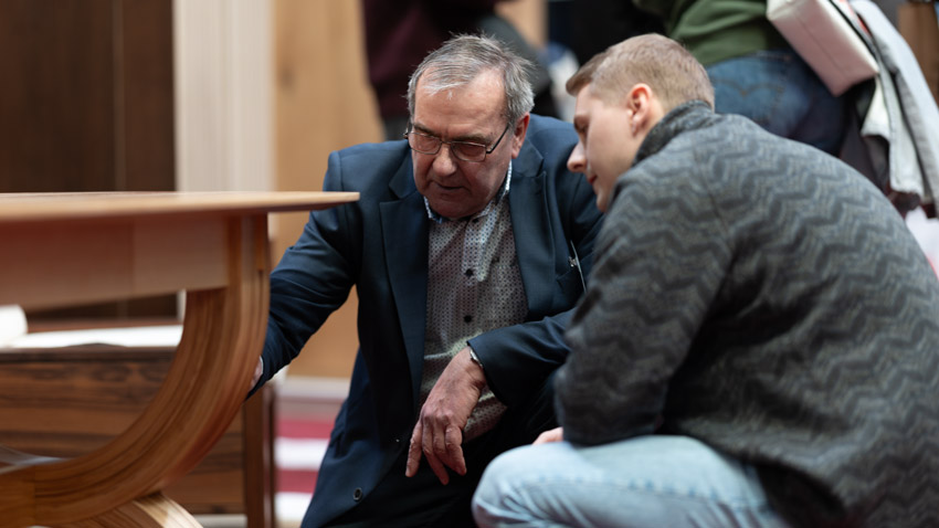 Zwei Männer begutachten gemeinsam ein Holzmöbelstück auf einer Ausstellung – Messebegleitung Möbel Erfurt