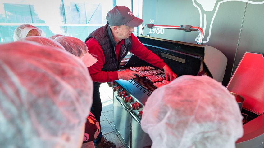 Mitarbeiter eines Fleischerei-Unternehmens grillt Würstchen an der Messestation – Reportagefotografie Messe Erfurt