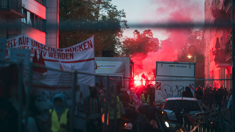 Rote Leuchtfackeln erhellen eine Straße in Berlin-Kreuzberg beim Abendumzug der Mai-Demonstration, Transparente im Vordergrund
