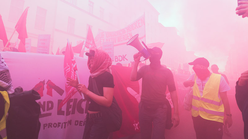 Demonstrierende beim Revolutionären 1. Mai in Berlin-Kreuzberg, eingehüllt in rosa Rauch, mit Transparenten und Megafon