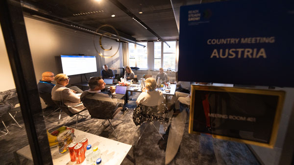 Blick durch eine Glastür auf ein Konferenzmeeting mit der Aufschrift „Country Meeting Austria“ – Fachleute im Gespräch.