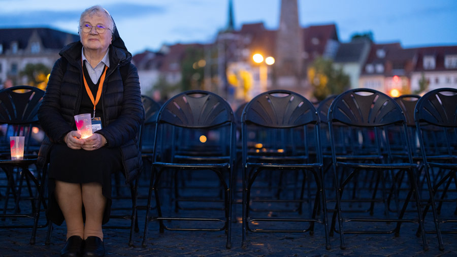ine Nonne sitzt bei Dämmerung auf einem leeren Platz in Erfurt und hält ein Teelicht in der Hand.